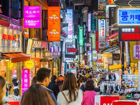 Een straatscène in Seoul met een mix van traditionele en moderne architectuur, neonreclames en veel voetgangers.