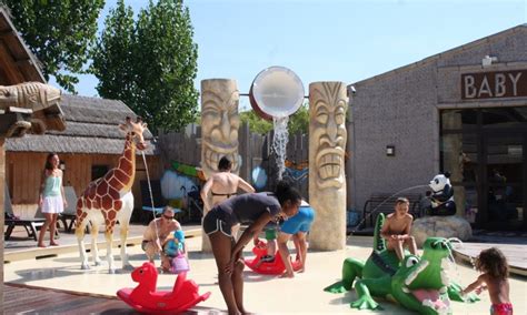 Impressie van het zwembadcomplex van Camping Kon Tiki met ligstoelen en palmbomen, en een apart kinderbad.