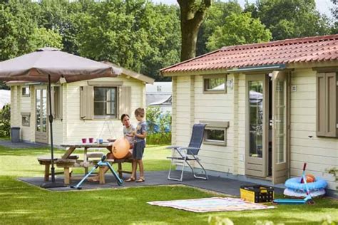 een overzichtsfoto van een gezellige camping met stacaravans, groenvoorzieningen en speelgelegenheid voor kinderen