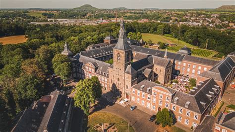 Buitenaanzicht van Abdij Rolduc met de karakteristieke architectuur omgeven door groen.