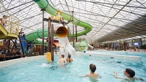 Interieur van een modern binnenzwembad op een vakantiepark met glijbanen en ligbedden.