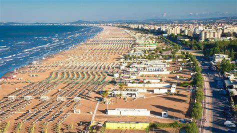Panoramische foto van het brede zandstrand van Rimini met strandtentjes en de Adriatische Zee op de achtergrond.