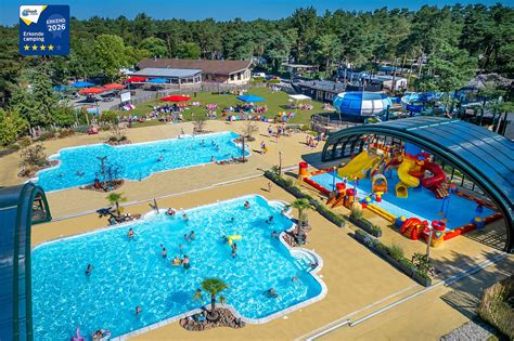 Vogelvluchtperspectief van Camping De Scheepsbel, omringd door groen, met het waterpark en de accommodaties zichtbaar.