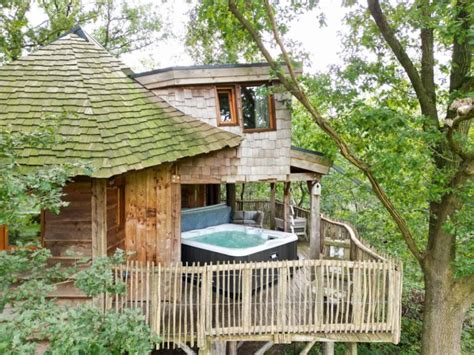 Houten chalet met een bubbelbad op het terras, omgeven door dennenbomen.