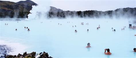 Mensen ontspannen in het turquoise water van een geothermisch bad, omringd door lavalandschap.