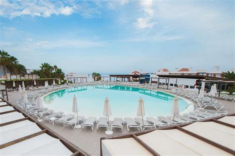 Een zwembad bij het Esencia de Fuerteventura hotel met ligbedden en parasols, omringd door groen.