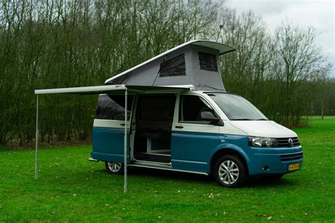 Een kleurrijke Volkswagen T1 camperbus geparkeerd op een camping aan zee.