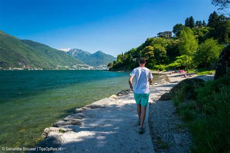 Een moderne trein die langs het Comomeer rijdt met op de achtergrond de bergen en het meer.