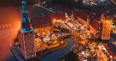 Een overzicht van de Adventsmarkt am Schloss Raesfeld met sfeervol verlichte kasteel en vele kraampjes.