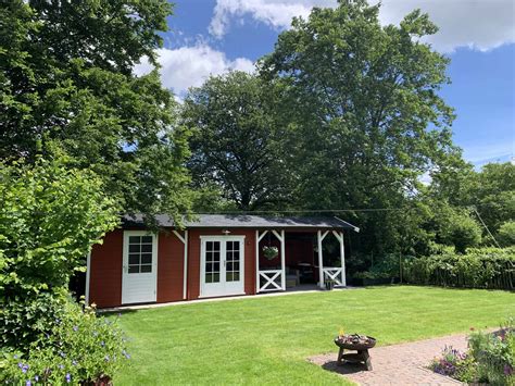 Een sfeervol rood Zweeds vakantiehuisje omgeven door groen, met een terras.