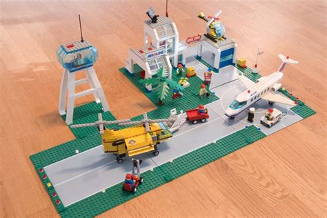 Illustratie van een gedetailleerde LEGO vliegveldplaat met vliegtuigen, verkeerstoren en infrastructuur.