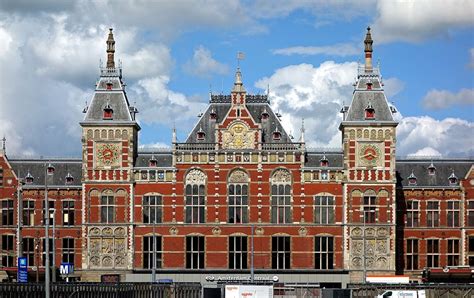 Buitenaanzicht van Amsterdam Centraal Station met de Damrak op de voorgrond.