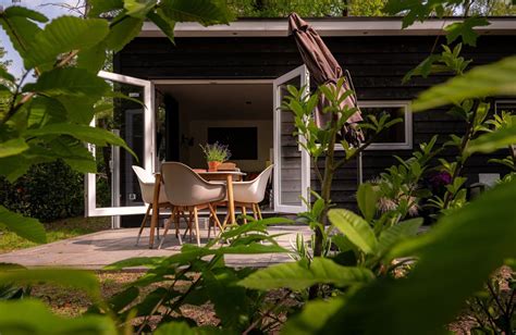 Een sfeervol 'tiny house' met een buitenterras en hot tub, omgeven door groen.