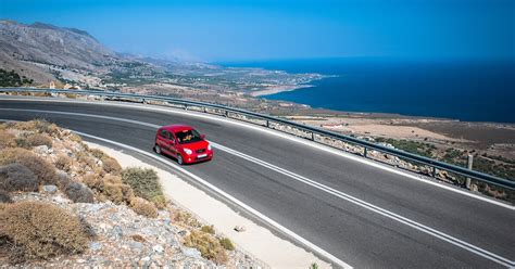 Vrolijk stel stapt uit huurauto op een zonnige parkeerplaats in de Algarve, met de oceaan op de achtergrond.