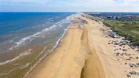 Een panoramisch uitzicht op het strand van Katwijk aan Zee met strandpaviljoens en de zee.