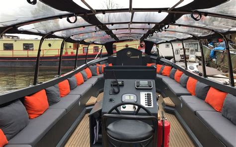 Luxe sloep vaart door de Amsterdamse grachten met historische panden op de achtergrond.