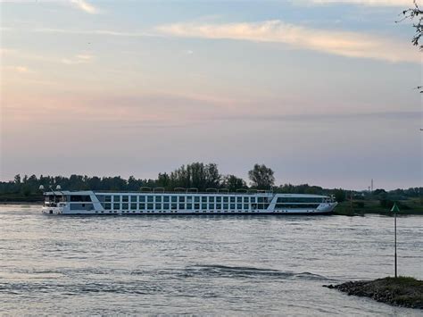 Een modern passagiersschip vaart op de Rijn met aan weerszijden groene oevers.
